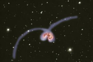 Deep-sky astrophotography of the colliding Antennae Galaxies (NGC 4038 and NGC 4039) in Corvus, showing two intersecting galactic cores surrounded by chaotic dust lanes, bright blue star clusters, and pink starburst regions.