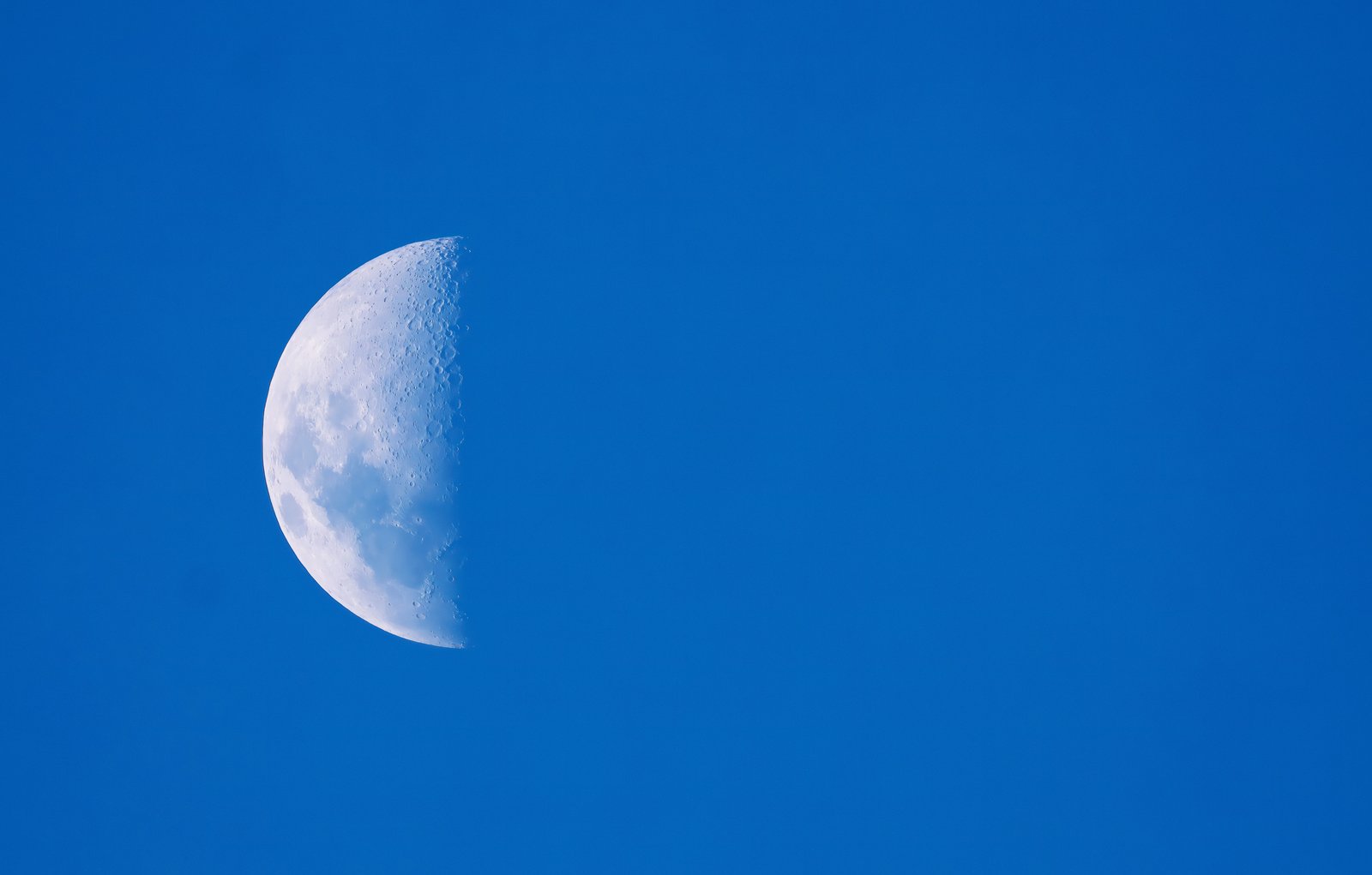A ghostly half moon during day time suspended in a bright blue afternoon sky, captured with the William Optics Pleiades 68. The premium, color-pure septuplet glass cuts right through atmospheric daytime glare, revealing crisp lunar maria and terminator craters against a perfectly clean cerulean backdrop.
