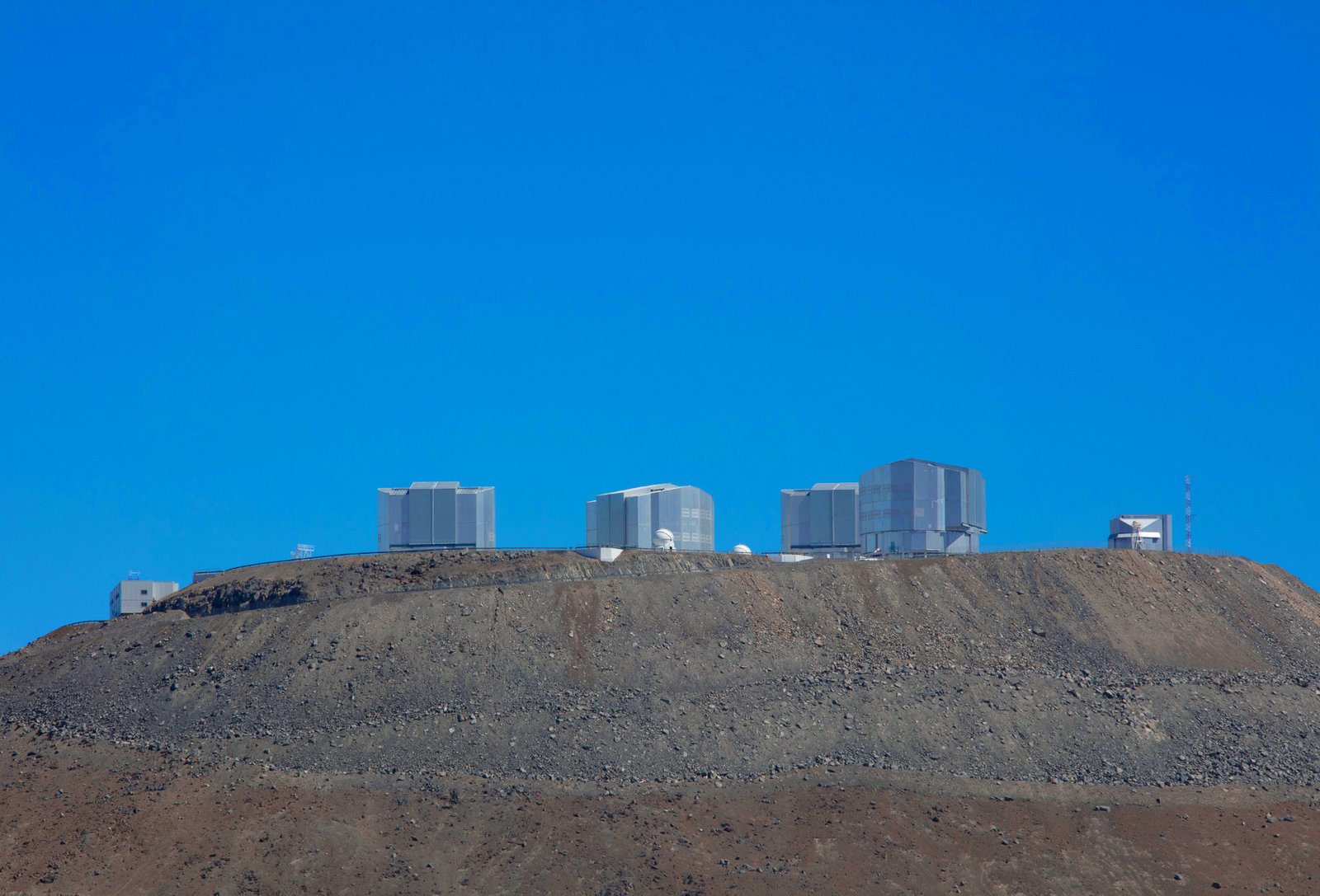 Perched above the clouds at 2,635 meters elevation. This wide-angle daytime panorama captures the four massive 8.2-meter Unit Telescopes of the Very Large Telescope (VLT) anchoring the summit of Cerro Paranal, standing out against the stark, otherworldly expanse of Chile's Atacama Desert.